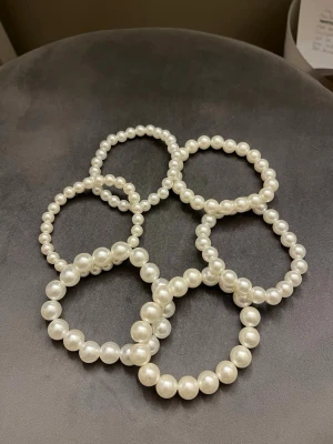 Pärlarmband  - Säljer flera elastiska armband med vita pärlor i plast. Armbanden har en klassisk rund form och passar perfekt för att ge en stilren och trendig touch till din outfit. Perfekt att bära flera tillsammans för en cool layering-effekt. Aldrig använda då de är lite för stora för mig.