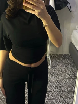 Svart croppad topp med kort ärm - Snygg svart croppad topp med korta ärmar och rund hals. Toppen har en tight passform och är perfekt för dig som gillar en enkel men trendig stil. Passar till både jeans och kjol för en cool look.