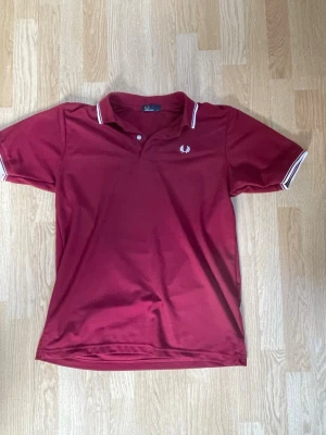 Vinröd Fred Perry pikétröja - Säljer en vinröd pikétröja från Fred Perry med klassisk krage och vita detaljer på krage och ärmslut. Riktigt fet tröja, tyvärr för stor för mig dock. Pris kan diskuteras.