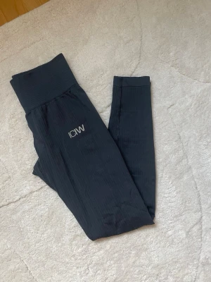 Svarta leggings från ICIW - Snygga svarta leggings från ICANIWILL med hög midja och ribbad linning. Diskret logga framtill. Stretchigt material som sitter skönt och följer kroppen. Perfekta för träning eller chill.