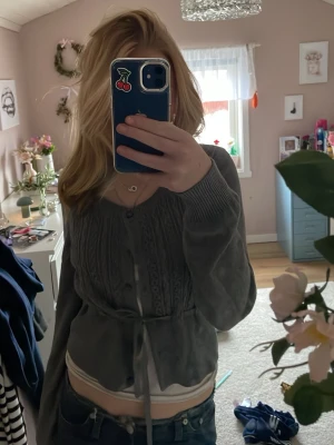 Grå stickad kofta från H&M - Snygg grå stickad kofta från H&M med knytband i midjan och dekorativa stickade detaljer framtill. Koftan har långa ärmar och ribbade muddar. Perfekt att slänga över en topp för en chill look.