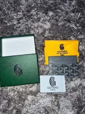 Plånbok - Säljer ett stilrent grått kortfodral från hm med det klassiska mönstret i vitt och svart. Kortfodralet har flera fack för kort och är tillverkat i exklusivt läder. Kommer med original ask, dustbag och certifikat.