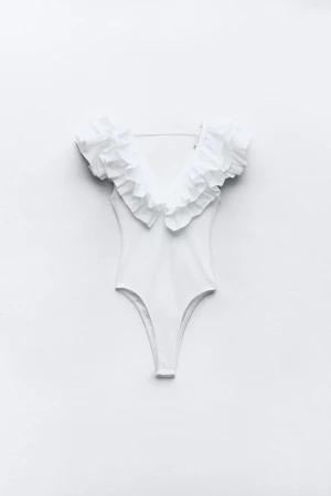 Vit baddräkt med volangdetaljer - Snygg vit baddräkt med djup V-ringning och stora volanger längs axlar och halsringning. Kroppsnära passform och högt skurna ben. Perfekt för dig som vill sticka ut på stranden med en trendig och feminin look.