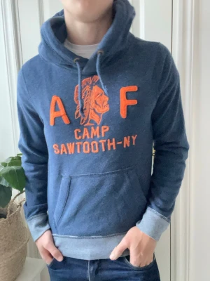 Abercrombie and fitch hoodie  - Abercrombie and fitch hoodie i blå med en orange logga. Väldigt najs och unik hoodie med ett snyggt mönster på ärmarna / slutet av tröjan. Väldigt najs och tung, sitter väldigt bra på modellen som är 180 cm 75 kg och bär Strlk S! 