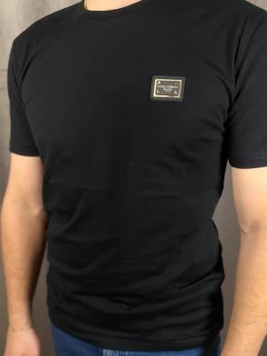 Svart Dolce & Gabbana t-shirt - Snygg svart t-shirt från Dolce & Gabbana med en metallbricka på bröstet där loggan står. T-shirten har rund halsringning och korta ärmar. Tillverkad i mjukt material som sitter skönt och stilrent.