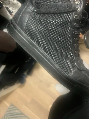 Svarta sneakers från Philipp Plein - Snygga svarta sneakers från Philipp Plein med coolt rutmönstrat och texturerat läder på sidorna. Högt skaft, svarta skosnören och diskret logga på sulan. Lyxig känsla och tillverkade i Italien – perfekt för dig som gillar statement-skor.