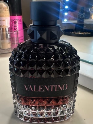 Valentino born in roma intense parfym - Snygg parfymflaska från Valentino med svart och rosa färgton. Flaskan har ett coolt nitat mönster och en svart etikett med rosa text. Korken är svart och dekorerad med pyramidformade nitar. Perfekt för dig som gillar lyxig design. 