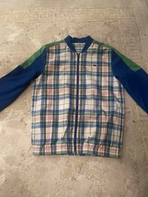 Rutig bomberjacka från Lacoste - Jacka från Lacoste med sköna byxor som matchar och en stor Lacoste logga på ryggen 