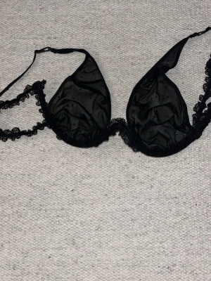 Svart mesh-bh med spetsdetaljer - Säljer en svart bh i transparent mesh med tunna axelband och fina spetsdetaljer längs kanterna. Bh:n har triangelformade glittriga kupor och är utan vaddering, vilket ger en lätt och luftig känsla. Perfekt för dig som gillar en stilren och sexig look.