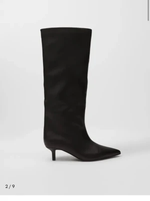Svarta knähöga boots med smal klack - Stilrena svarta knähöga boots i slätt läder med spetsig tå och låg smal klack. Klassisk och trendig siluett som passar till många olika looks. Perfekta för dig som vill ha en edgy men elegant vibe. Från Nelly i storlek 38 endast använda 2. Som nya i skicket. Köpta för 800kr