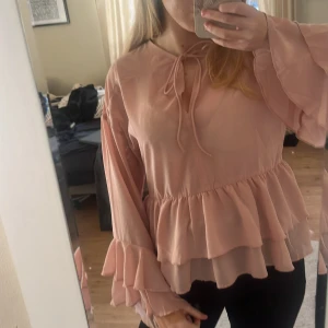 Rosa volangblus - Supersöt ljusrosa blus från H&M Divided i storlek XXS, dock skulle jag säga att den passar större då jag är en Xs-S. Blusen har långa ärmar med dubbla volanger, knytband vid halsen och peplumvolang nedtill. Materialet är lätt och flowy polyester, perfekt till både romantiska middagar och tjejkvällar. Den har även en fläck på ena volangen men detta är inget som märks!