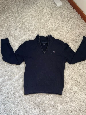 Marinblå stickad half zip-tröja Lexington - Marinblå stickad tröja från Lexington med half zip och liten logga på bröstet. Tröjan har lång ärm, ribbade muddar och klassisk krage. Perfekt för dig som gillar stilrena och tidlösa plagg.