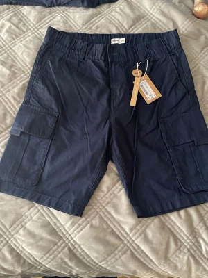 Mörkblå cargoshorts från Dobber - Snygga mörkblå cargoshorts från Dobber med praktiska sidofickor och bälteshällor. Tillverkade i mjuk bomull som känns skön mot huden. Perfekta för dig som gillar en avslappnad och funktionell stil.