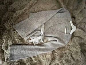 Grå omlottkofta med knytband - Mysig grå omlottkofta från Gina med knytband i midjan. Koftan har lång ärm och ribbstickade detaljer vid ärmslut och halsringning. Perfekt för lager-på-lager och enkel att styla till olika outfits.