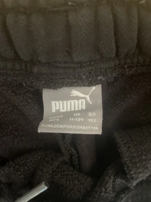 Svarta sweatpants från Puma - Säljer ett par svarta sweatpants från Puma med resår i midjan och två sidofickor. Byxorna har en vit Puma-logga tryckt på ena benet och är tillverkade i mjukt, bekvämt material. Perfekta för träning eller chill.