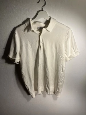 Vit pikétröja från MNG - Klassisk vit pikétröja från MNG med korta ärmar och krage. Tröjan har knäppning framtill med två knappar och är tillverkad i ett mjukt, tunt stickat matetial som ger en avslappnad look. 