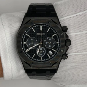 Svart seiko AP klocka med länkarmband - Stilren svart Seiko kronografklocka med robust länkarmband i metall. Klockan har en åttakantig boett som Liknar AP, svart urtavla med rutmönster, tre subdials och vita detaljer. Datumvisning vid klockan fyra och tydliga indexmarkeringar. Perfekt accessoar för en modern look.