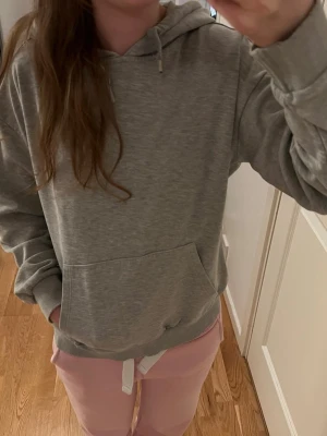 Grå hoodie med huva - Mysig grå hoodie med huva och känguruficka framtill. Klassisk modell med ribbade muddar vid ärmslut och nederkant. Perfekt för chill dagar eller när du vill ha en enkel och stilren look. Ett av snörelocken har åkt av annars är den jättefin. från Gina tricot Nypris ca 300kr. 