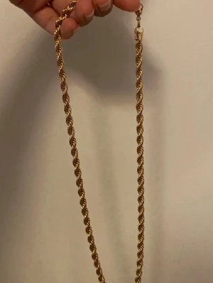 Guldfärgat tvinnat halsband - Snyggt halsband i guldfärg med tvinnad kedja som ger en cool och trendig look. Halsbandet har en klassisk karbinhake och passar perfekt till att lyfta vilken outfit som helst. Materialet ser ut att vara metall med en glansig finish.