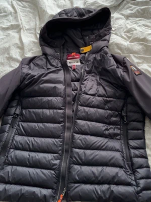 Svart dunjacka från Parajumpers - Snygg svart dunjacka/cardigan från Parajumpers med huva och dragkedja. Jackan har quiltad design, två sidofickor med dragkedja och en patch med logga på ärmen. Perfekt för kalla vinterdagar och riktigt stilren look. 9/10 skick. 