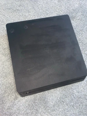 PlayStation 4 Slim svart konsol - Säljer en svart PlayStation 4 Slim från Sony. Konsolen har en stilren, rektangulär design med rundade hörn och matt finish. Tillverkad i plast och passar perfekt för gaming och underhållning hemma.