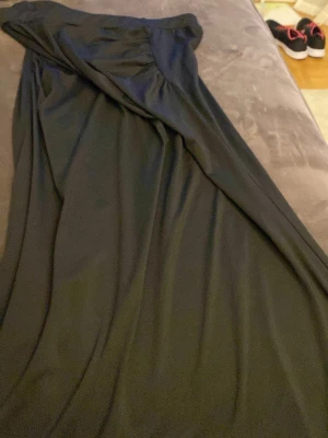 Svart kjol  med drapering - Elegant svart kjol med snygg drapering och lätt rynkade detaljer upptill. Kjolen har en klassisk och tidlös design som passar perfekt till speciella tillfällen. Materialet känns mjukt och följsamt mot kroppen.