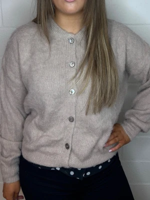 Beige fluffig kofta med knappar - Mysig beige kofta med fluffig känsla och rund halsringning. Koftan har långa ärmar och stängs med fyra stora knappar framtill. Perfekt för lager på lager och enkel att matcha till olika outfits.