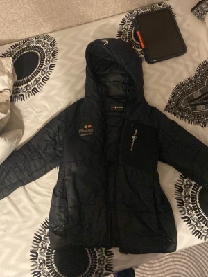 Svart dunjacka från Sail racing  - Pris kan diskuteras Säljer en svart dunjacka från sail racing  med huva och dragkedja. Jackan har broderad logga sail racing på bröstet och praktiska fickor. Perfekt för kalla vinterdagar och har en sportig look.