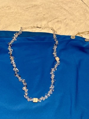 Halsband med klara pärlor och silverdetaljer - Snyggt halsband med klara pärlor i oregelbunden form och två fyrkantiga silverfärgade detaljer. Halsbandet har ett klassiskt lås och passar perfekt för att ge din outfit lite extra bling.oanvänd 