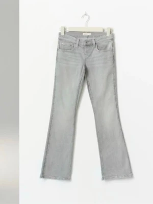 Grå bootcut jeans från Gina tricot - Snygga grå bootcut jeans från Gina med klassisk femficksdesign och dekorativa sömmar på bakfickorna. Jeansen har låg midja och är tillverkade i mjuk denim med lite stretch för extra komfort.