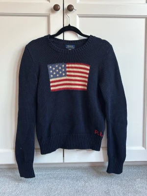 Mörkblå stickad tröja Polo Ralph Lauren - Mörkblå stickad tröja från Polo Ralph Lauren med amerikansk flagga på bröstet och RL-broderi vid nederkanten. Storleken är 16 år/xl för barn. ❤️