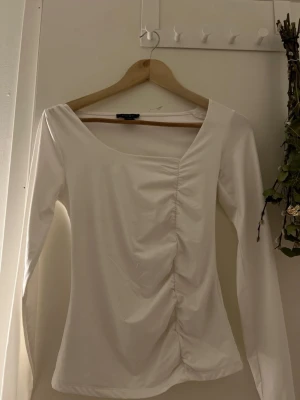 Vit långärmad topp från Amisu - Säljer en vit långärmad topp från Amisu med snygg rynkning framtill. Toppen har en bred, rundad urringning och är tillverkad i ett mjukt, stretchigt material som sitter bekvämt på kroppen. Perfekt att styla med jeans eller kjol.