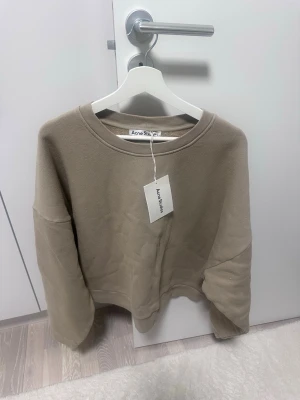 Beige sweatshirt från Acne Studios - Säljer en helt ny Snygg beige sweatshirt från Acne Studios. Tröjan har diskret logo på ryggen och är tillverkad i mjukt bomullsmaterial. Perfekt för en stilren och enkel look. Ny pris: 4252 kr 