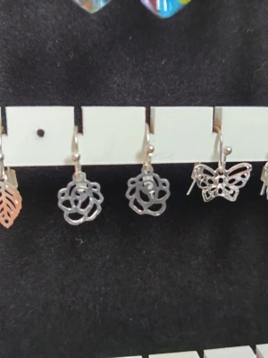 Silvriga örhängen med blommor och fjäril - Säljer ett set med silvriga örhängen i olika former: blad, rosor och fjäril. Alla örhängen har en tunn, utskuren design som ger en lätt och stilren känsla. Perfekta för dig som gillar unika och detaljerade accessoarer.