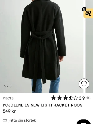 Svart kappa från Pieces med knytskärp - Stilren svart kappa från Pieces med klassisk krage och knytskärp i midjan. Kappan har raka ärmar, två stora fickor framtill och en rak passform. Perfekt för dig som vill ha en enkel men snygg look till vardags. Materialet ser ut att vara mjukt och lätt.