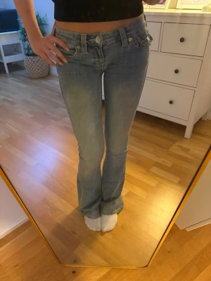 Ljusblå bootcut jeans True Religion-Joey - Säljer ett par ljusblå bootcut jeans från True Religion med klassisk femficksdesign och låg midja. Jeansen har detaljerade sömmar, perfekta för en avslappnad och trendig look. Original pris-1299kr. Hålet där bak är enkelt att sy ihop med symaskin eller för hand!! Syns inte tydligt enligt mig. 