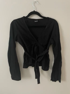 Svart omlottopp från Gina Tricot - Säljer en svart omlottopp från Gina Tricot med långa ärmar och knytband i midjan. Vid snabbt köp går pris att diskuteras🥰