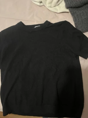 Svart stickad kortärmad tröja Gina Tricot - En svart, stickad kortärmad tröja från Gina Tricot. Tröjan har en enkel och clean design med rund halsringning och rak passform. Perfekt att styla med jeans eller kjol för en chill look.