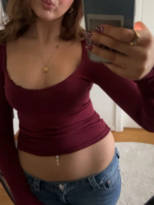Vinröd långärmad topp med djup ringning - Säljer en vinröd långärmad topp med djup, rundad ringning och diskret spetskant. Modellen är tight och croppad, perfekt att styla med jeans eller kjol. Materialet känns mjukt och stretchigt, troligen bomull eller polyester. Supersnygg färg som sticker ut!