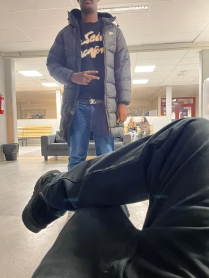 Svart lång pufferjacka med huva - Säljer en svart lång pufferjacka från Nike med huva. Jackan är quiltad och har en clean look med diskret logga på bröstet. Perfekt för kalla dagar när du vill hålla dig varm och ändå se stilren ut. Passar dig som gillar en lite oversized vibe.