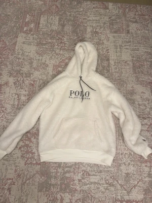 Polo Ralph Lauren teddy hoodie – vit - Säljer en supermjuk och varm hoodie från Polo Ralph Lauren i teddy/fleece-material. Vit färg med svart POLO-logga framtill. Bekväm modell med huva, känguruficka och ribbade muddar.