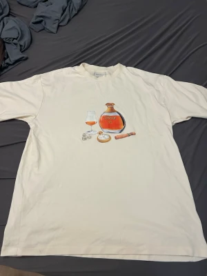  t-shirt Drôle de Monsieur L - Säljer en creme färgad t-shirt från Drôle de Monsieur i storlek L. Framsidan har ett tryck med konjakflaska, glas, tärningar, fickur och cigarr. Oversized passform och rund hals. Kommer med original dustbag.