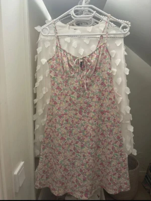 Blommig sommarklänning Gina Tricot - Söt kort blommig klänning från Gina Tricot i storlek XXS. Klänningen har justerbara smala axelband och en liten knytning framtill. Färgerna går i rosa, grön, gul och vit, och materialet är lätt och skönt för varma dagar. Den är verkligen i ett jättebra skick!!!!!!!!!!