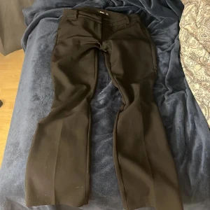 Svarta bootcut kostymbyxor BikBok - Säljer ett par svarta kostymbyxor från BikBok i storlek 38. Byxorna har bootcut-modell med vida ben, bälteshällor och stängs med både hake och knapp. Byxorna är lågmidjade. Materialet är mjukt och har en lätt glansig finish som ger en snygg look.