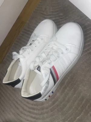 Vita sneakers med ränder och snörning - Snygga vita sneakers med svarta, röda och grå detaljer. Skorna är helt nya och passar inte men kunde inte lämna tillbaka de. 