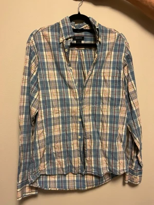 Gant skjorta  - Säljer en klassisk rutig skjorta från GANT i blå, vit, gul och röd färg. Skjortan är i bomull, har lång ärm, bröstficka och knappar framtill. Regular fit och tillverkad i Portugal. Perfekt för dig som gillar avslappnad men snygg stil.