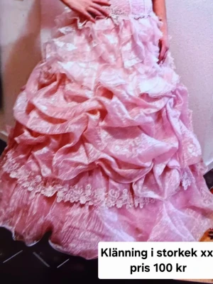 Rosa långklänning med spets och volanger - Säljer en pampig rosa långklänning med flera lager volanger och dekorativa spetsdetaljer. Klänningen har en romantisk look med mycket tyg och struktur, perfekt för speciella tillfällen. Passar dig som vill sticka ut och älskar prinsesskänsla.
