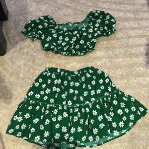 Grön blommig croppad blus - Supersöt grön croppad blus med vita blommor och puffiga korta ärmar. Toppen har resår vid midjan och ärmarna för en bekväm passform. Perfekt för varma dagar och ger en riktigt somrig vibe.