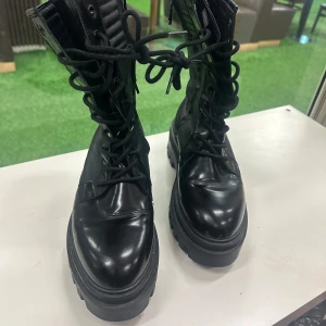 Svarta boots från Calvin Klein Jeans - Säljer ett par svarta boots från Calvin Klein Jeans med grov platt sula och snörning hela vägen upp. Skorna är tillverkade i skinn och har märkets logga på sidan, plösen och undersidan. Riktigt chunky och coola med rund tå och högt skaft.