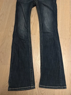 Bootcut jeans från Miss Me, mörkblå - Snygga mörkblå bootcut jeans från Miss Me med kontrasterande vita sömmar och dekorativa knappar på fickorna. Jeansen har broderade detaljer på bakfickorna och klassisk femficksdesign. Materialet är jeans med en skön passform och låg midja. Priset kan diskuteras!!